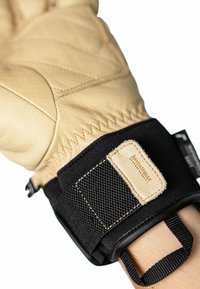 Tan leren handschoen met zwart textielen polsband. Beschikt over versterkte stiksels en klittenbandsluiting voor een veilige pasvorm.