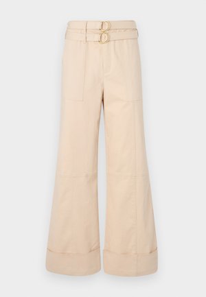 Pantalones de pierna ancha beige con cintura alta, que presentan dos hebillas circulares doradas y bolsillos en la parte frontal; tela de algodón lisa con puños enrollados.
