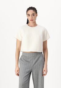 Cropped short-sleeve top in textured cream fabric, paired with gray high-waisted patterned trousers, featuring a straight-leg cut.