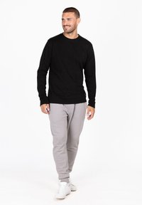 Schwarzes Langarmhemd kombiniert mit grauen Sweatpants, aus weichem Stoff. Das Hemd hat einen Rundhalsausschnitt und enganliegende Bündchen.