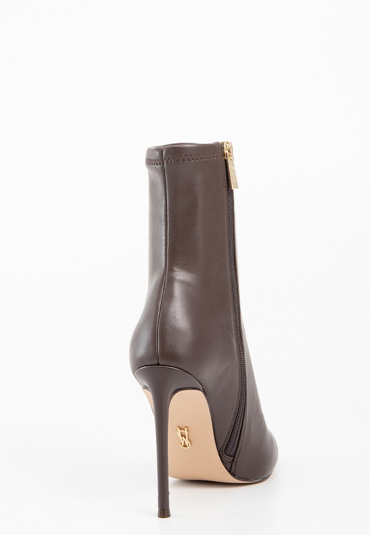 Bottines à talons hauts en cuir marron avec fermeture éclair latérale et accents en matériel doré ; elles présentent une texture lisse et un design à bout pointu.
