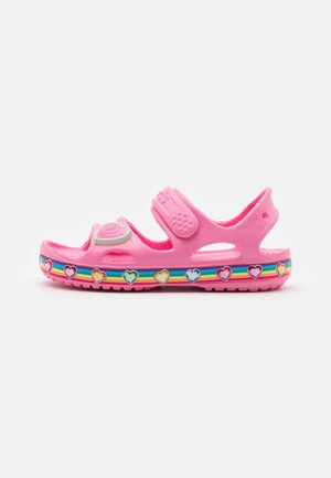 Sandale enfant rose avec brides réglables, semelle rayée arc-en-ciel et décorations en forme de cœurs multicolores le long du bord.