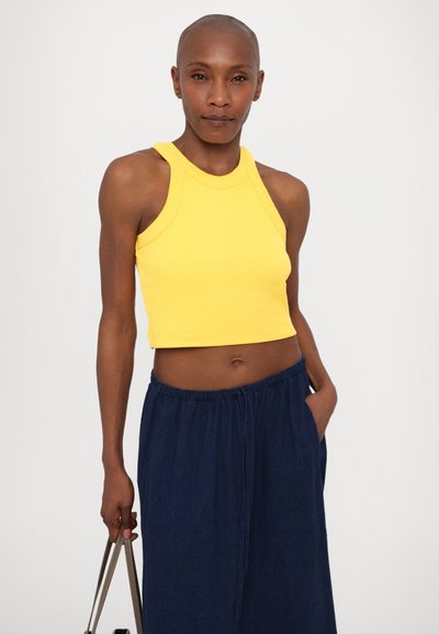 Geel geribbeld crop-top met halternekdesign, gecombineerd met navyblauwe losse broek met een elastische tailleband en zakken.