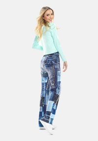 Helle blaue Langarmbluse kombiniert mit blauem Denim-Hosen mit Patchwork, die unterschiedliche Texturen und Muster aufweisen, abgerundet mit weißen Sneakers.