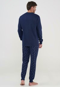 Conjunto de ropa de casa de algodón azul marino que incluye una camiseta de manga larga y pantalones decorados con motivos de estrellas blancas. Puños elásticos en los tobillos.