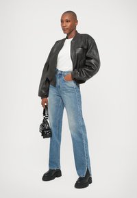 Svart läderbombarjacka, vit t-shirt, ljusblå denimjeans med sidoflikar, och svarta kängor med tjock sula. Accessoarerna inkluderar en liten svart väska.