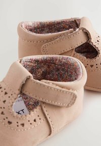 Chaussures en cuir rose pâle avec des découpes, une bande Velcro et une doublure à motifs floraux. Elles présentent un bout rond et des accents de couture.