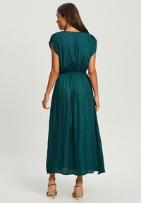Teal maxi dress with short sleeves, elastic waistband, and flowing fabric. Smooth texture and simple back design, featuring a small neck closure.