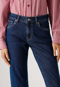 Σκούρα μπλε τζιν με κανονική εφαρμογή, που διαθέτουν εμπρόσθιες τσέπες, αντίθετη ραφή και κλασικό κούμπωμα με κουμπί στη μέση.