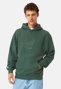 Grön hoodie med en framficka i kängurustil och en justerbar huva. Har präglad texten "Ärlighet Regler" på bröstet. Tillverkad av bomullsblandad tyg.
