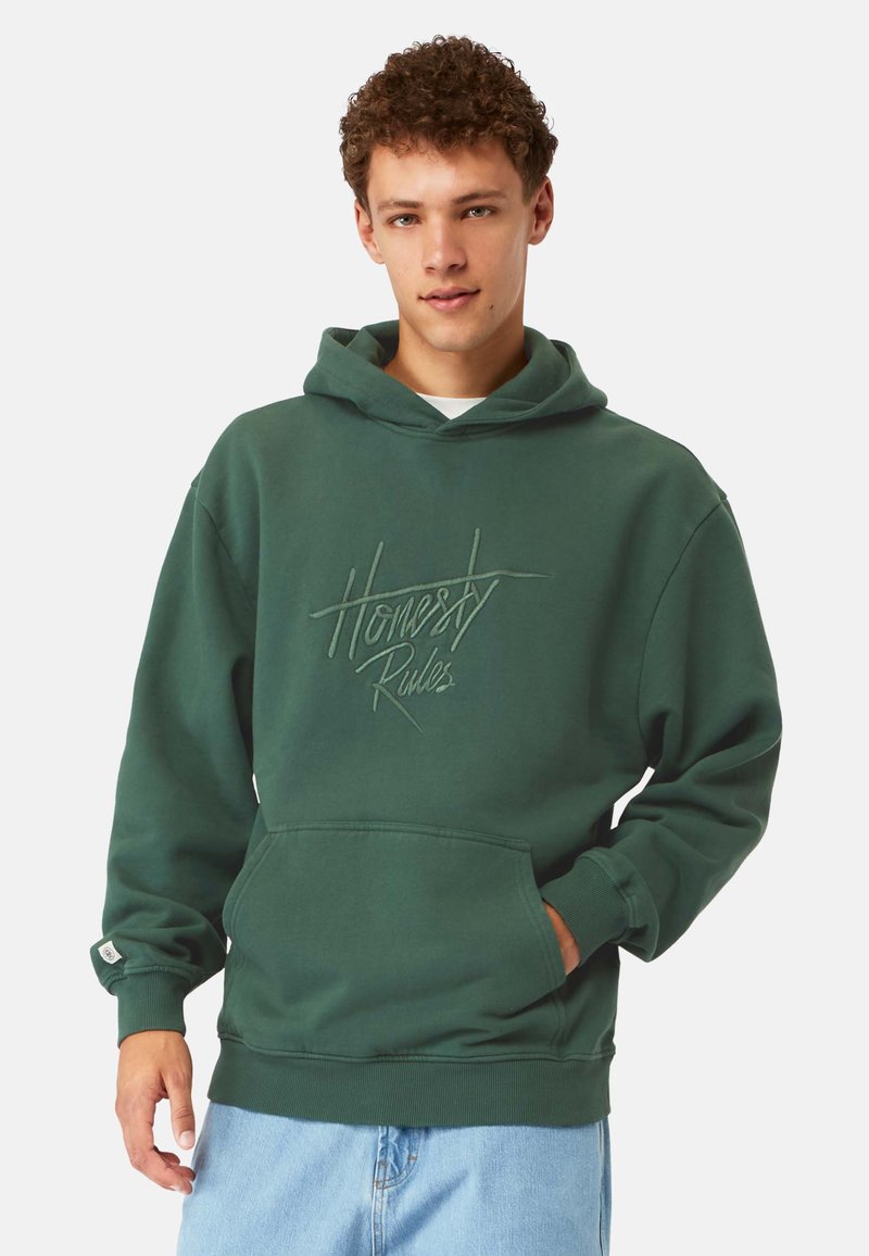 Grön hoodie med en framficka i kängurustil och en justerbar huva. Har präglad texten "Ärlighet Regler" på bröstet. Tillverkad av bomullsblandad tyg.