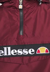 Maroon lightweight jacket with a black embroidered logo band and contrasting zipper. Hood with drawstring and subtle sheen.