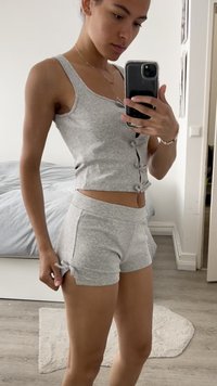 Conjunto de roupa de lazer cinza de duas peças, com top cropped e detalhes em botão, e calções curtos com laços, exibido contra um fundo neutro.