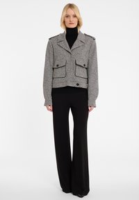 Grijze gestructureerde cropped jas met dubbele opgestikte zakken en schouder epauletten, gecombineerd met zwarte wijde broekspijpen. Gladde stoffen afwerking.