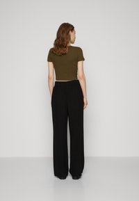 Olivengrønn avkortet t-skjorte kombinert med svarte, vide bukser. Glatt tekstur og elastisk midje på buksene, minimalistisk design.
