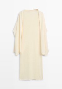 Longue robe tricotée de couleur crème avec des manches larges et amples, présentée à plat sur un fond blanc.