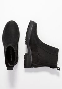 Musta mokkanahka nilkkasaappaat elastisilla sivupaneeleilla, pyöreällä varvalla ja karkealla kumipohjalla. Varustettu vetotarralla, joka helpottaa pukemista.