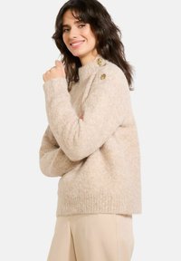 Beidzis adīts džemperis ar augstu apkakli un ribotām aprocēm. Iezīmē dekoratīvas pogas uz pleca. Tekstūrēts, mīksts audums.