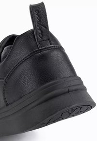 Baskets noires avec un dessus en cuir texturé, un talon incurvé et une languette. La semelle extérieure présente un motif de relief pour l'adhérence.