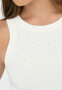 Hvid ribbet tanktop med rund halsudskæring og spredte små sølvdekorationer for tekstur. Nærbillede af stofdetaljen.