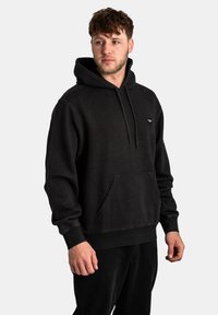 Black hoodie with a front pocket, drawstring hood, and ribbed cuffs. Features subtle stitching details and a small logo on the chest.