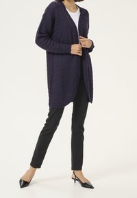 Fioletowy dzianinowy kardigan o fakturowanym wzorze, z otwartym przodem i długimi rękawami, w połączeniu z czarnymi dopasowanymi spodniami i czarnymi butami na obcasie.