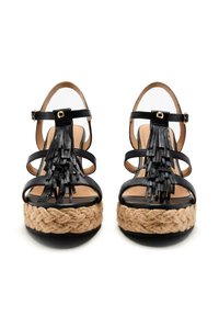 Sandalias negras con tiras y plataforma de yute trenzado. Cuentan con flecos de cuero y correas ajustables en el tobillo con acentos de hardware dorado.