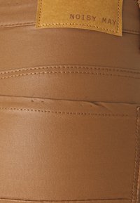 Tela de imitación de cuero marrón con una textura suave, que presenta costuras visibles y una etiqueta marrón claro embellecida con "NOISY MAY."