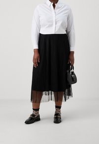 Vit skjorta med knappar, svart plisserad midikjol, svarta loafers och strumpor med hjärtan. Liten svart handväska med metallisk detaljer.