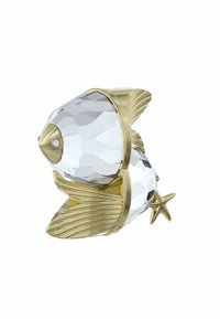 Figurki rybki z kryształu z złotymi akcentami, wielobocznym przezroczystym korpusem, szczegółowymi płetwami i ogonem w kształcie gwiazdy. Zawiera mały dekoracyjny kamień szlachetny.