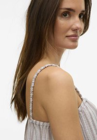 Top color beige chiaro con spalline sottili e raccolte, realizzato in un tessuto testurizzato con sottili righe e una vestibilità rilassata, presentato sul profilo di un modello.