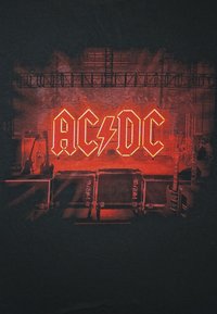 Sceneoppsett med rødt neon AC/DC-logo, gitarer på begge sider og utstyrskasser foran, opplyst av rødt lys.