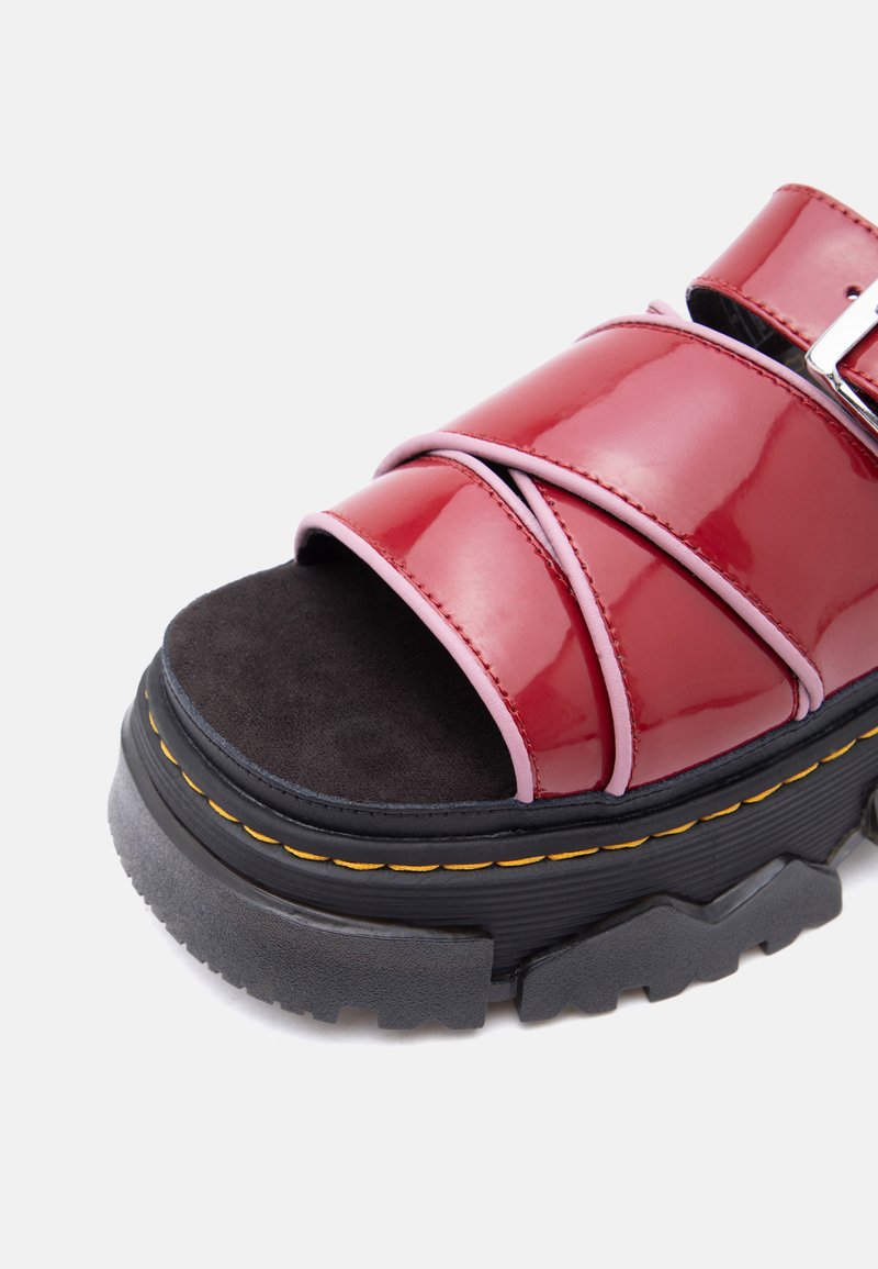 Sandalo platform nero robusto con cinturini rossi lucidi, rifinitura rosa, punta aperta e cuciture gialle lungo la suola.