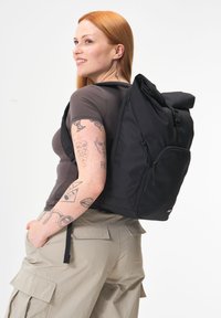 Schwarzer Rolltop-Rucksack mit einer vorderen Reißverschlusstasche und seitlichem Zugang. Hergestellt aus strapazierfähigem Material, ausgestattet mit verstellbaren Tragegurten und einem schlanken Design.