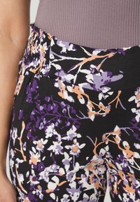 Bloemmotief broeken met een zwarte basis, voorzien van paarse en oranje bloemen. Elastische tailleband met een gladde textuur en een aansluitend ontwerp.