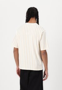 Kortærmet T-shirt i creme med smalle orange lodrette striber; letvægtsstof, afslappet pasform, rund halsudskæring og søm i siderne.