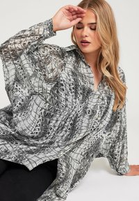 Lekka koszula w czarno-białe wzory z szerokimi rękawami, z zapięciem na guziki z przodu oraz teksturowanym wzorem przypominającym skórę gadów.