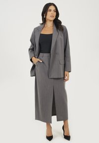 Szary żakiet i dopasowana spódnica z rozcięciem. Żakiet ma luźny krój i wyraziste klapy; materiał ma delikatną teksturę. Pod spodem czarna bluzka.