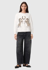 Λευκό φούτερ με δύο λεπτομερείς γραφικές παραστάσεις αλόγων και πετάλου, συνδυασμένο με μαύρο τζιν φαρδιάς γραμμής και μαύρα μοκασίνια. Απλός σχεδιασμός.