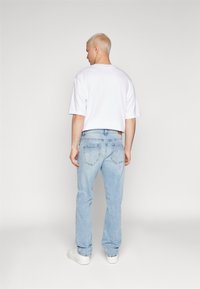 White short-sleeve t-shirt, light blue straight-leg jeans, visible tag at waist, plain design, and minimalistic white sneakers.