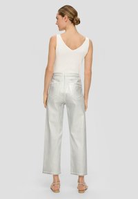 Helle graue, hoch taillierte Jeans mit geradem Bein, ausgestattet mit Gesäßtaschen und ausgefransten Säumen, kombiniert mit einem weißen ärmellosen Top.