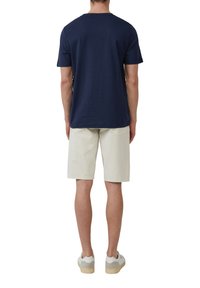 Marineblauw katoenen T-shirt met korte mouwen en ronde hals, gecombineerd met lichtbeige shorts. Model draagt witte en grijze sneakers met een gestructureerde zool.