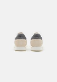 Sneaker bianche con accenti grigi e beige, caratterizzate da un mix di pelle e suede, forma arrotondata e dettaglio testurizzato sul tallone.