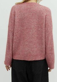 Rosa gestrickter Pullover mit lässiger Passform, überschnittenen Schultern und geripptem Saum. Weiche Textur, leicht fuzzy Optik und keine sichtbaren Muster.