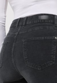 Grau Cord Hosen mit Slim Fit, strukturiertem Oberflächenstoff und gesteppten Akzenten. Die hinteren Taschen sind rechteckig und haben einen Knopfdetails.