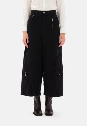 Pantaloni neri a gamba larga realizzati in misto cotone. Le caratteristiche includono una tasca con zip in argento, una grande tasca laterale e dettagli delle cuciture distintivi.