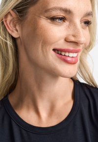 Záběr na tvář osoby se světle blond vlasy. Subjekt má světlou pleť s pihami a má na sobě černou košili. Rty mají růžový nádech.