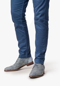 Scarpe da uomo light blue a fantasia con finitura testurizzata, abbinate a pantaloni fitted blu scuro, che mettono in mostra un design elegante e moderno.