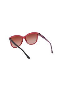 Lunettes de soleil rouges, semi-transparentes, avec des verres dégradés marron. Les branches noires sont ornées d'un accent violet à motifs. Forme œil de chat avec une finition brillante.
