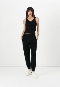 Svart cropped tank top med trekantdetalj, kombinert med svarte tapered sweatpants. Modellen har på seg hvite joggesko. Rent, minimalistisk design.